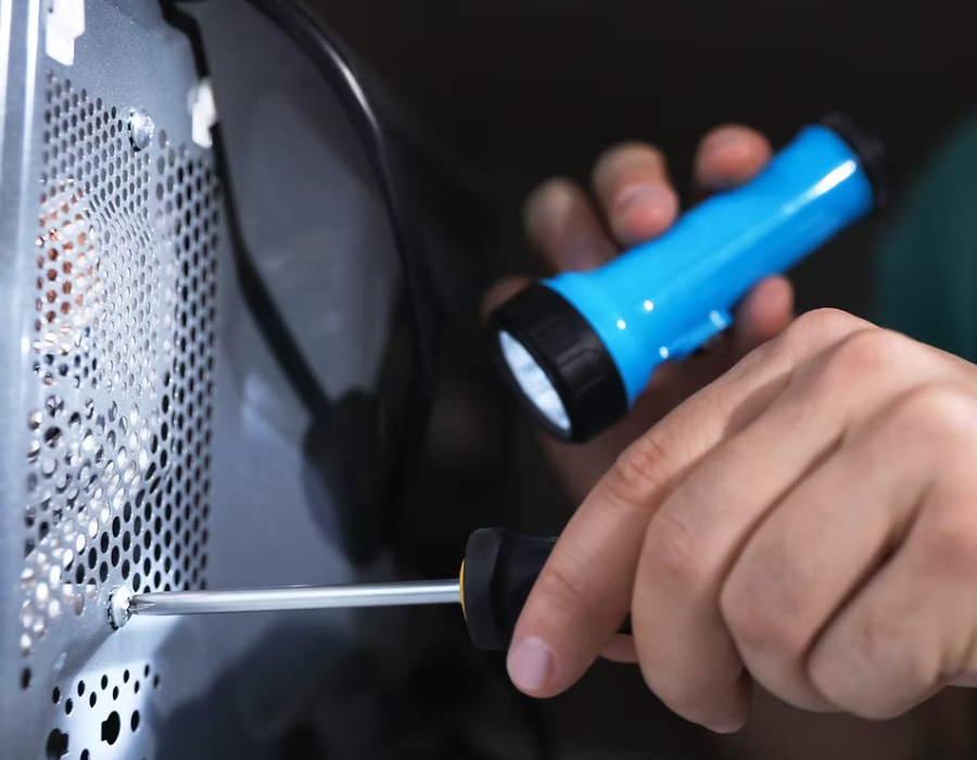 Engineer repairing an appliance with a torch and screwdriver